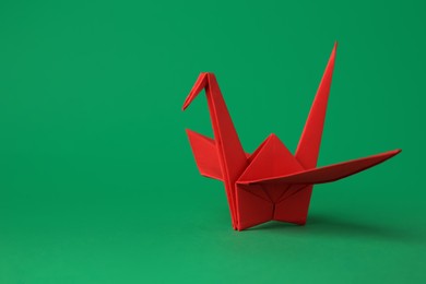Photo of Red paper origami crane on green background, space for text
