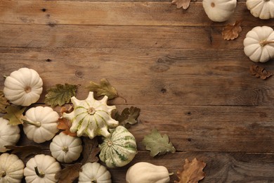 Photo of Different fresh ripe pumpkins and dry leaves on wooden table, flat lay. Space for text