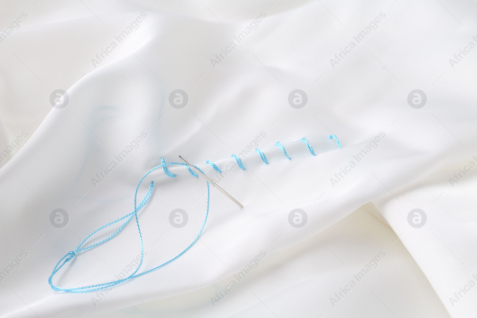 Photo of Sewing needle with thread and stitches on white cloth, closeup