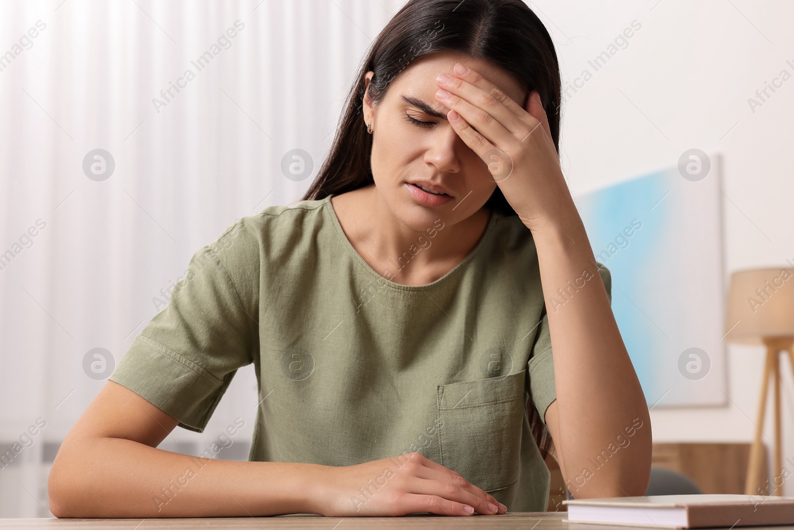 Photo of Sad woman suffering from headache at wooden table indoors