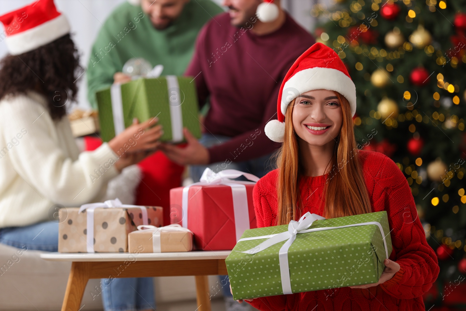 Photo of Christmas celebration in circle of friends. Happy young woman with gift box at home, selective focus