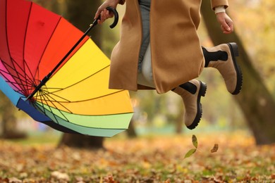 Photo of Woman with rainbow umbrella jumping in autumn park, closeup