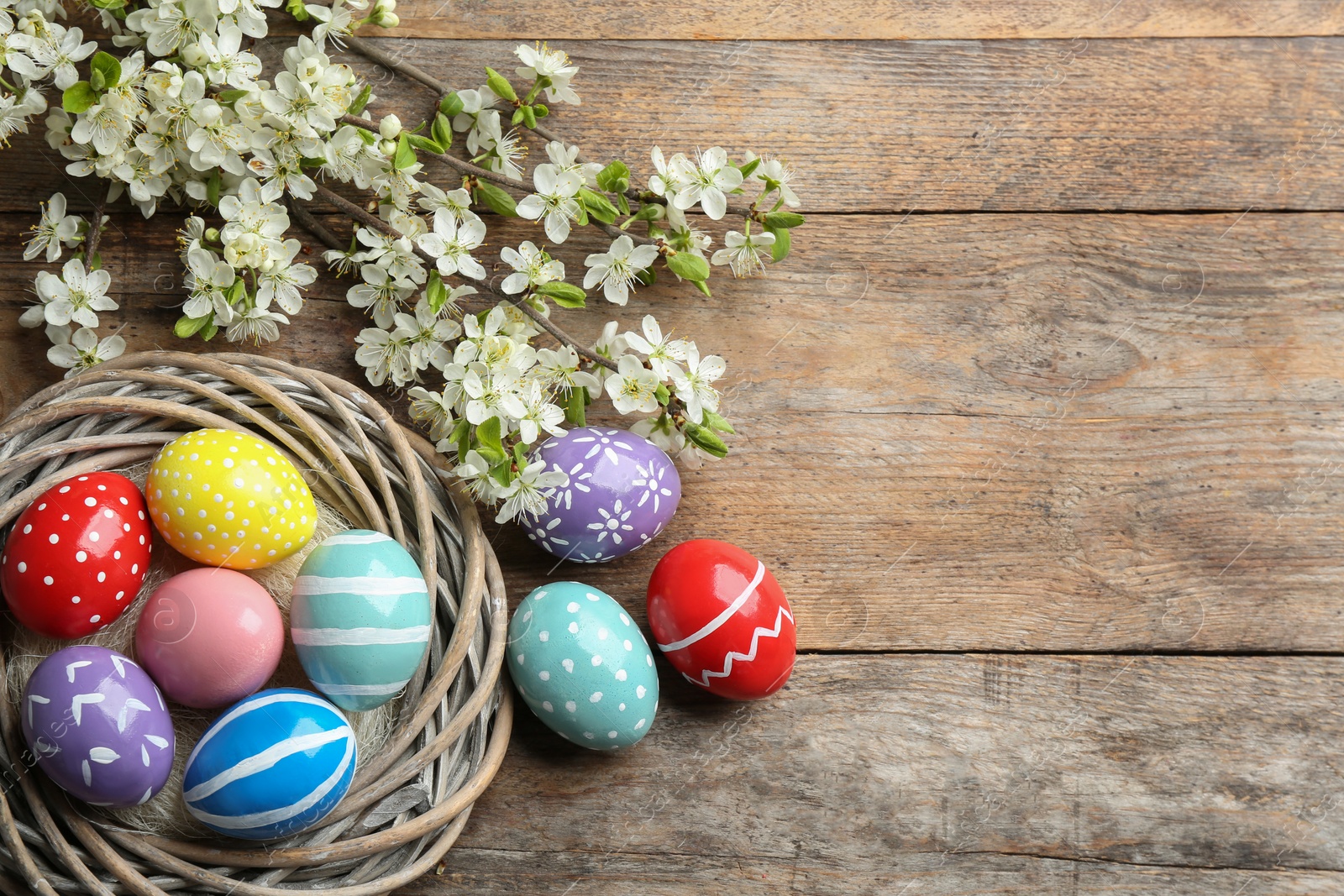 Photo of Flat lay composition with painted Easter eggs and blossoming branches on wooden background. Space for text