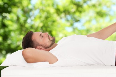 Image of Man lying on comfortable mattress against blurred green background, bokeh effect. Sleep well - stay healthy