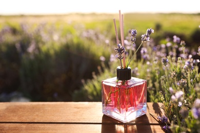 Photo of Bottle of air freshener on wooden table in lavender field. Space for text
