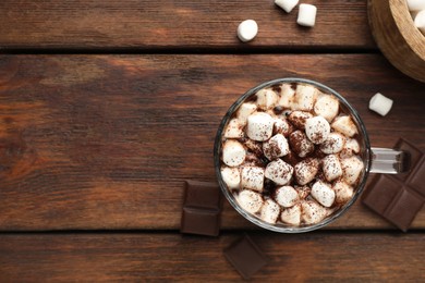 Cup of aromatic hot chocolate with marshmallows and cocoa powder on wooden table, flat lay. Space for text