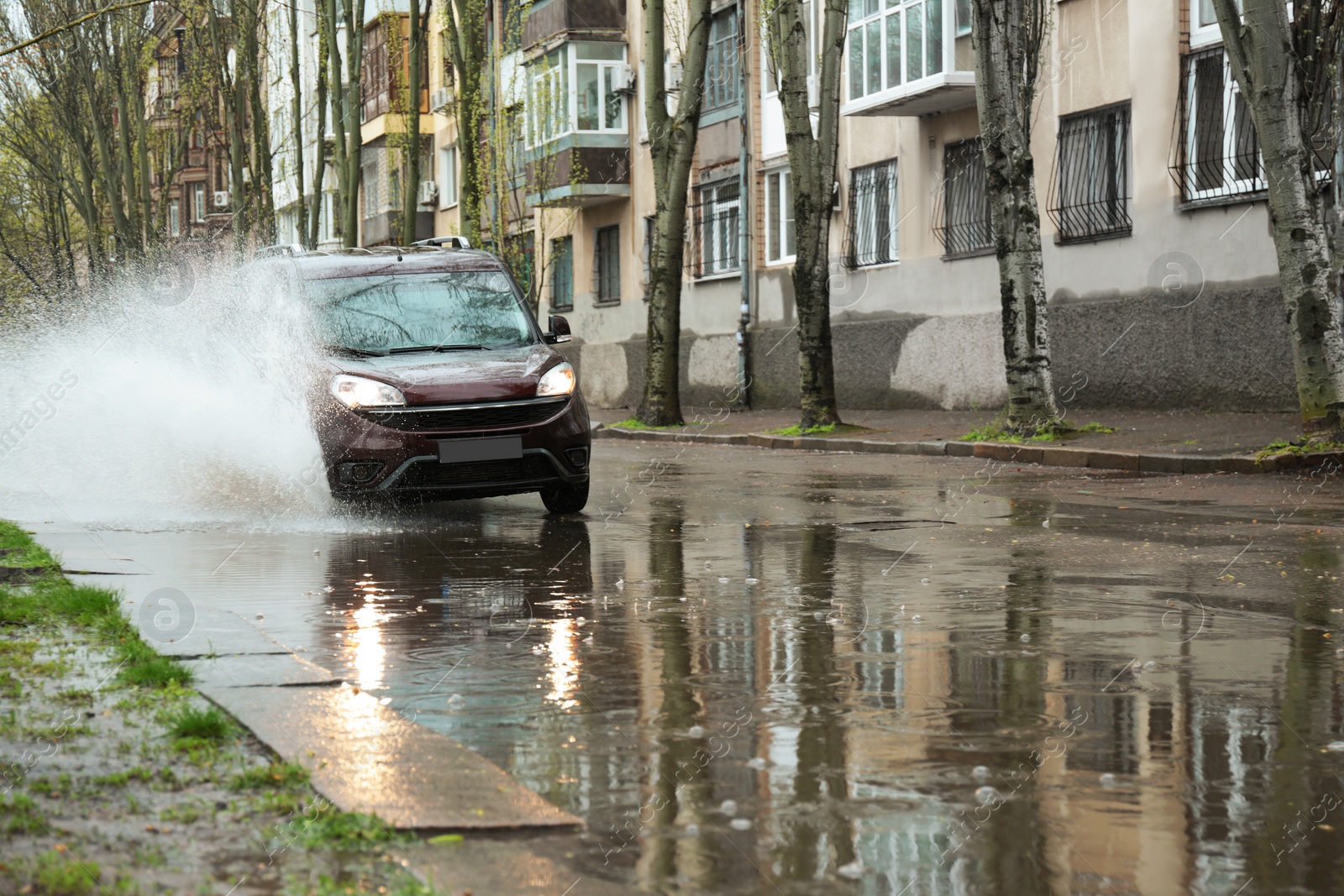 Photo of Car driving through large puddle outdoors on rainy day