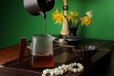 Pouring freshly brewed pu-erh tea into pitcher on wooden table