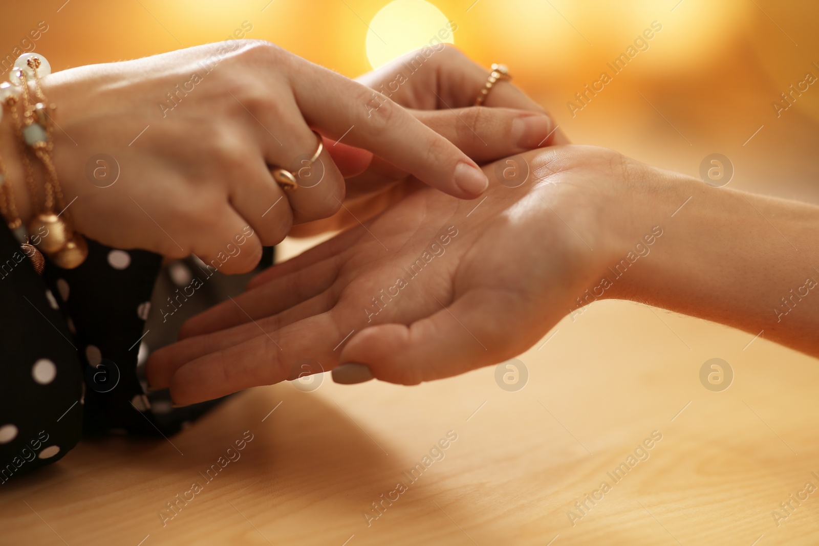 Photo of Chiromancer reading lines on woman's palm at table, closeup