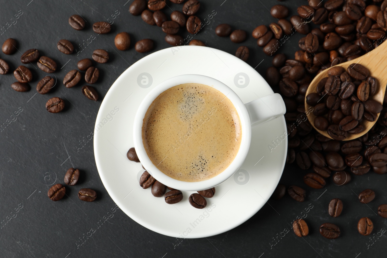Photo of Cup of aromatic coffee and beans on black table, flat lay
