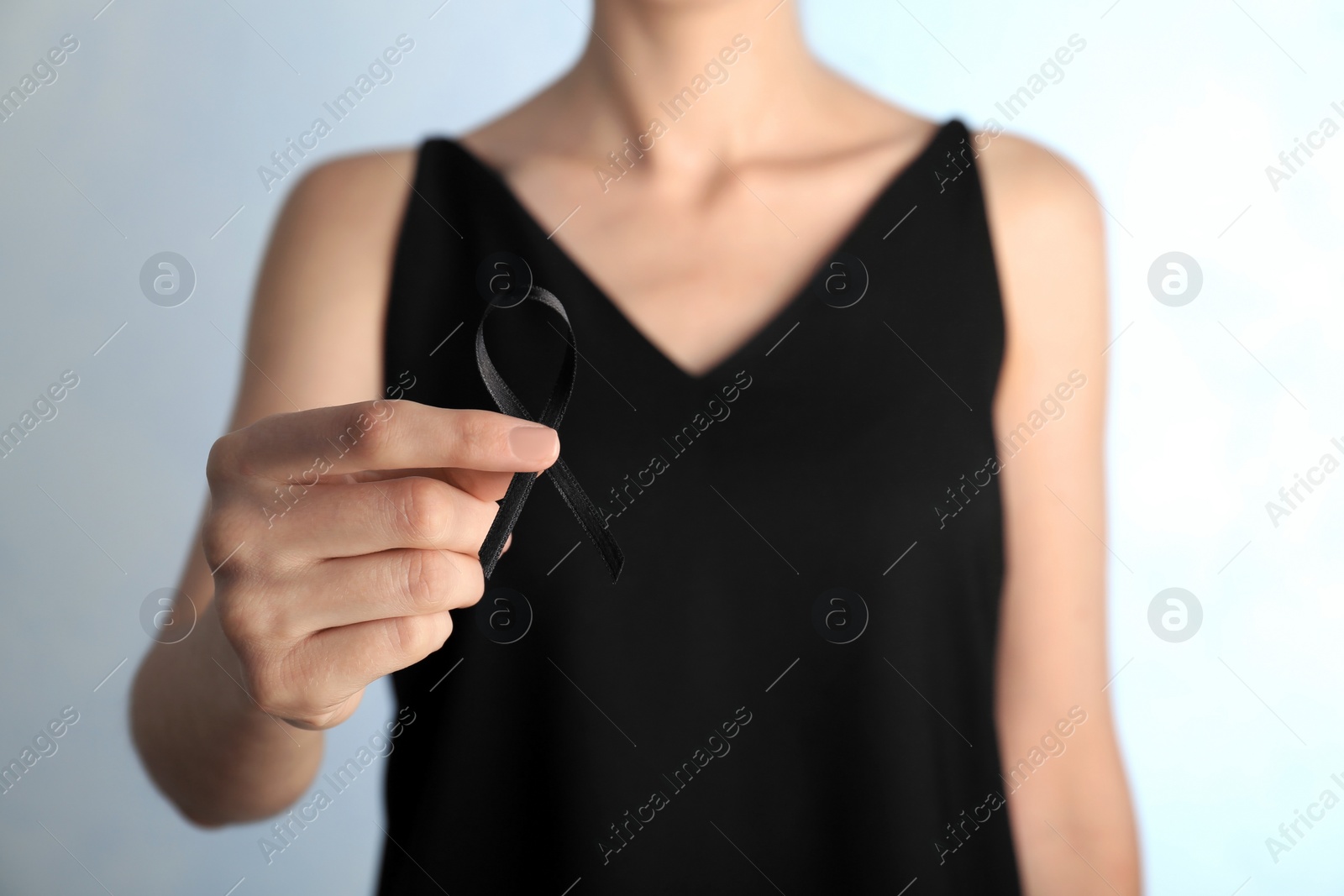 Photo of Woman holding black ribbon on light background, closeup. Funeral symbol