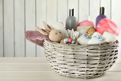 Photo of Wicker basket with baby cosmetics and accessories on white wooden table