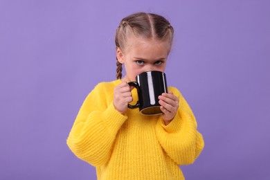 Photo of Cute girl drinking beverage from black ceramic mug on violet background
