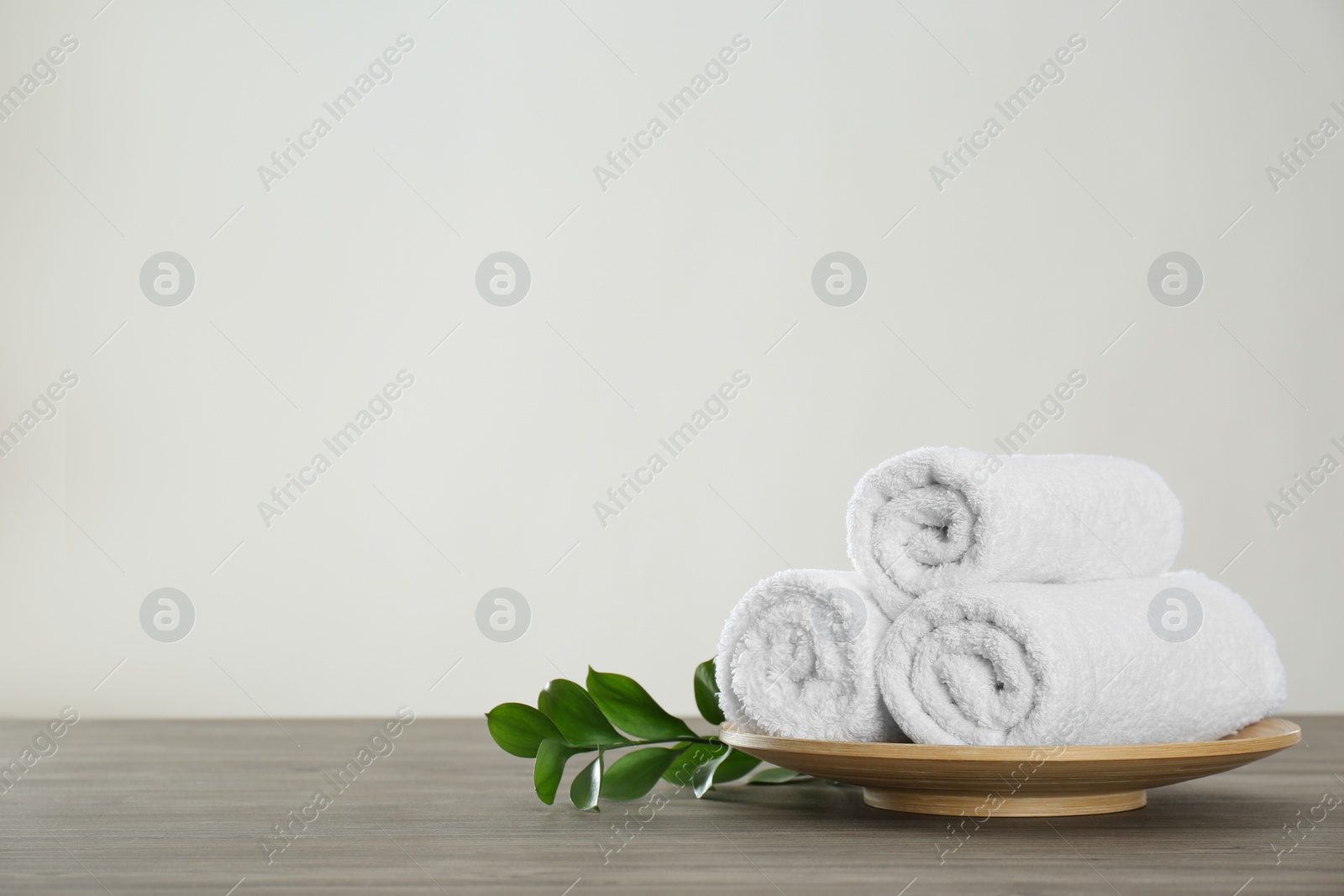 Photo of Fresh rolled towels and green leaves on grey wooden table. Space for text