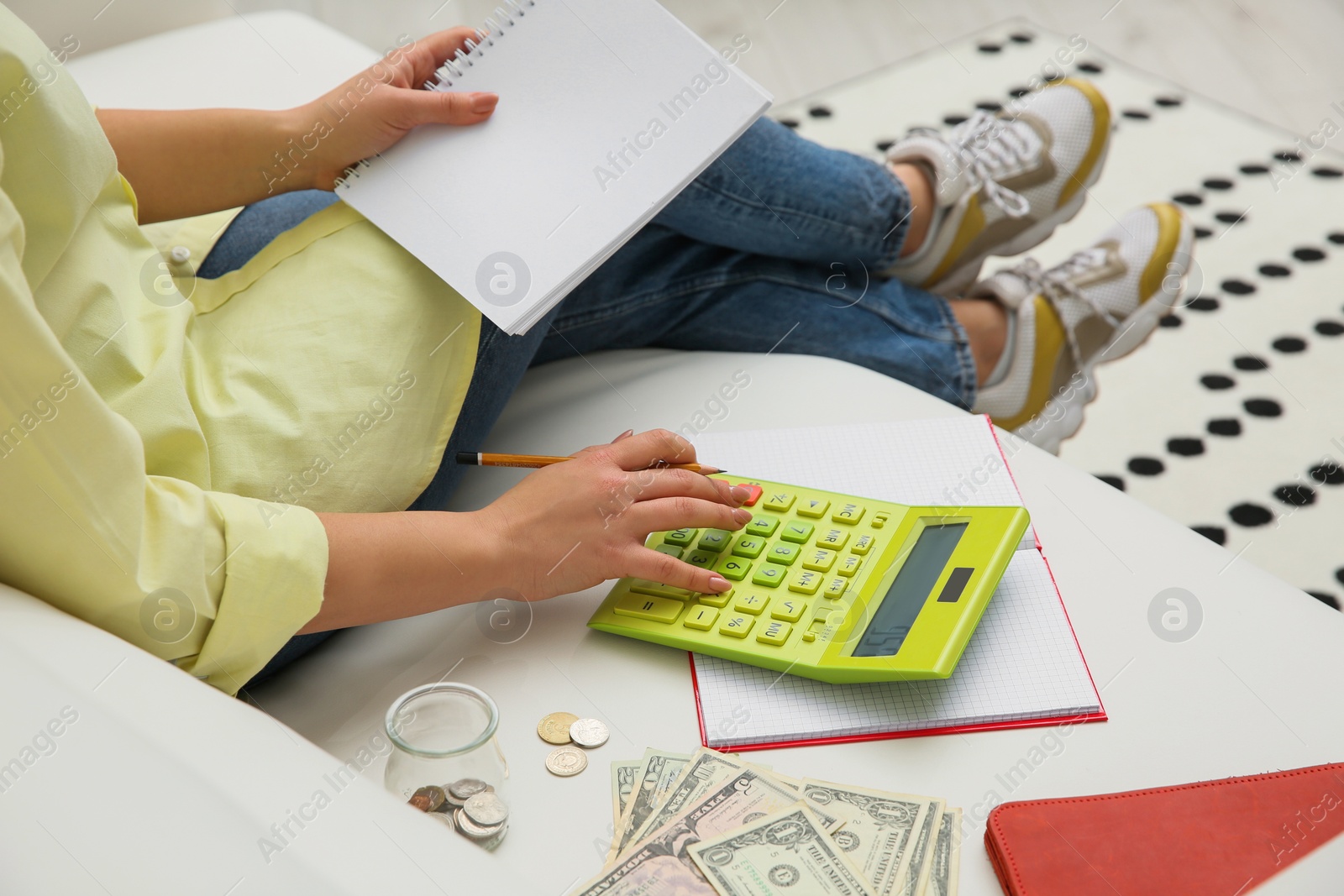 Photo of Young woman counting money with calculator on sofa indoors, closeup