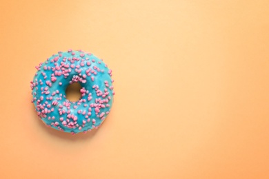 Delicious glazed doughnut with sprinkles on color background, top view