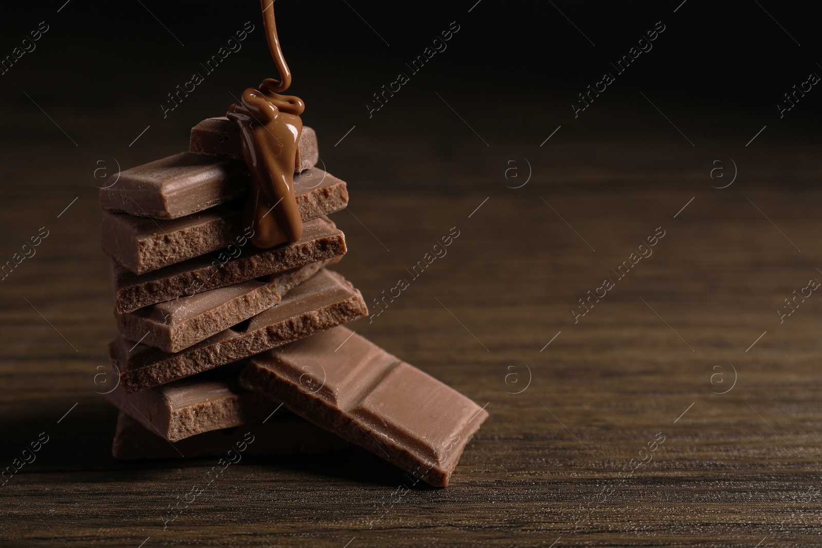 Photo of Pouring tasty milk chocolate paste onto pieces on wooden table, closeup. Space for text