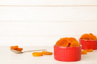 Photo of Red bowl with dried apricots on table, space for text. Healthy fruit