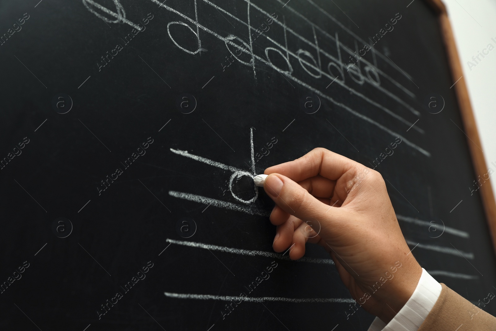 Photo of Teacher writing music notes with chalk on blackboard, closeup