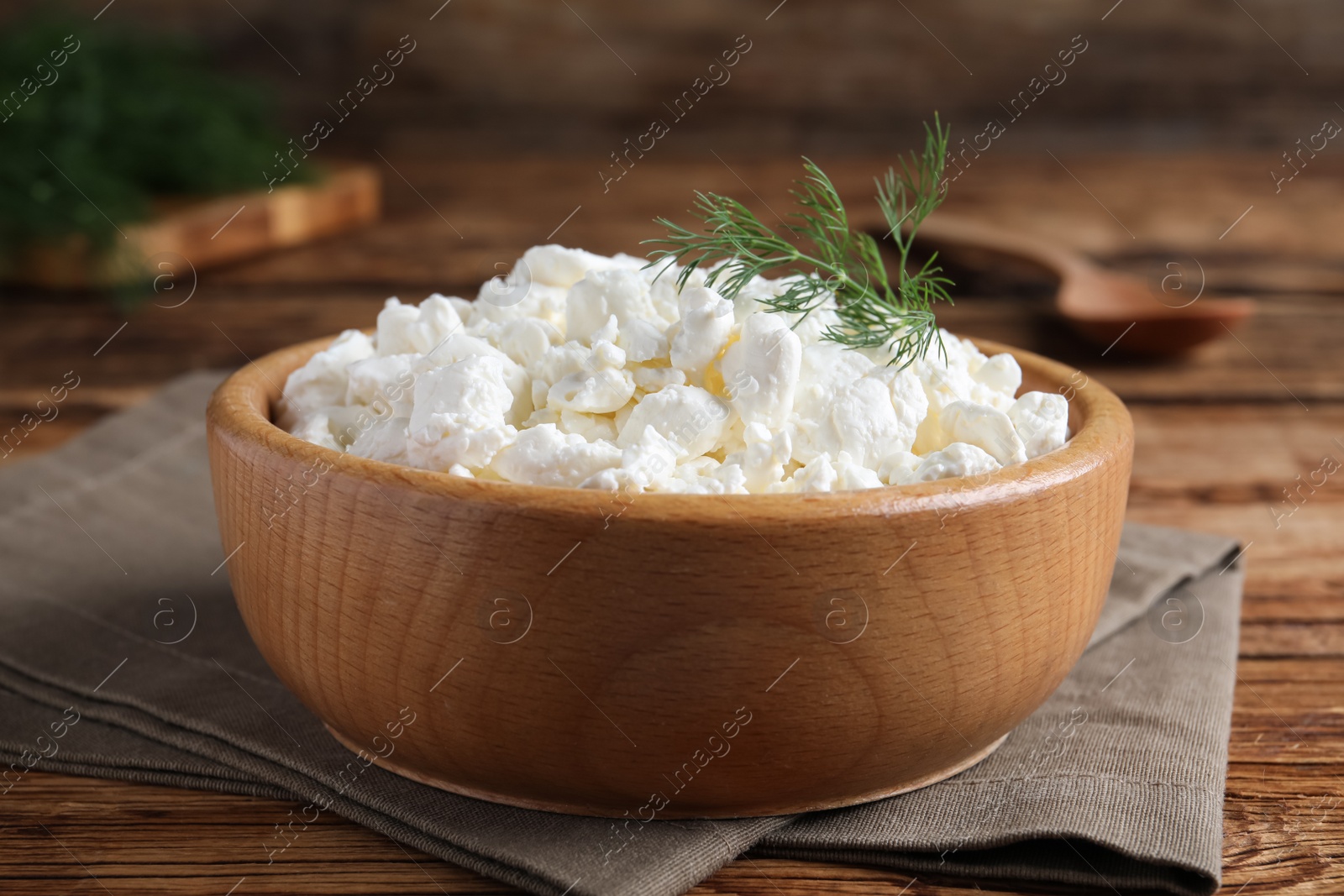 Photo of Fresh cottage cheese with dill in wooden bowl on table, closeup