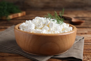 Photo of Fresh cottage cheese with dill in wooden bowl on table, closeup