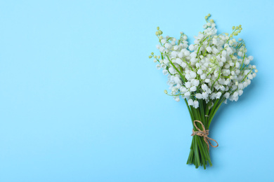 Beautiful lily of the valley flowers on light blue background, top view. Space for text