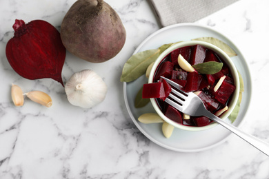 Photo of Pickled beets with garlic in bowl on white marble table, flat lay