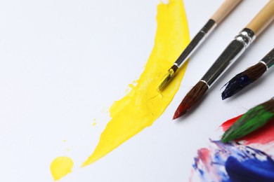 Photo of Brushes with different paints and strokes on white background, closeup. Space for text