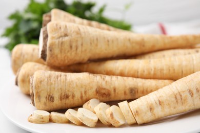 Photo of Whole and cut parsley roots on table, closeup