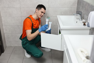 Photo of Smiling plumber wearing protective gloves repairing sink in bathroom