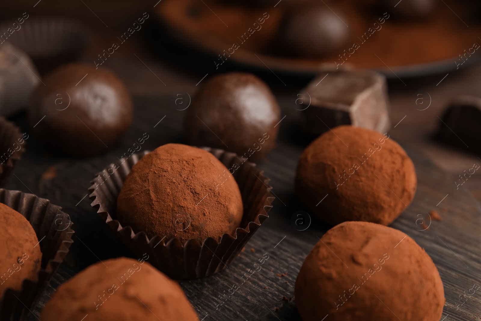 Photo of Delicious chocolate truffles powdered with cocoa on wooden board, closeup