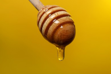 Photo of Pouring honey from dipper against golden background, closeup