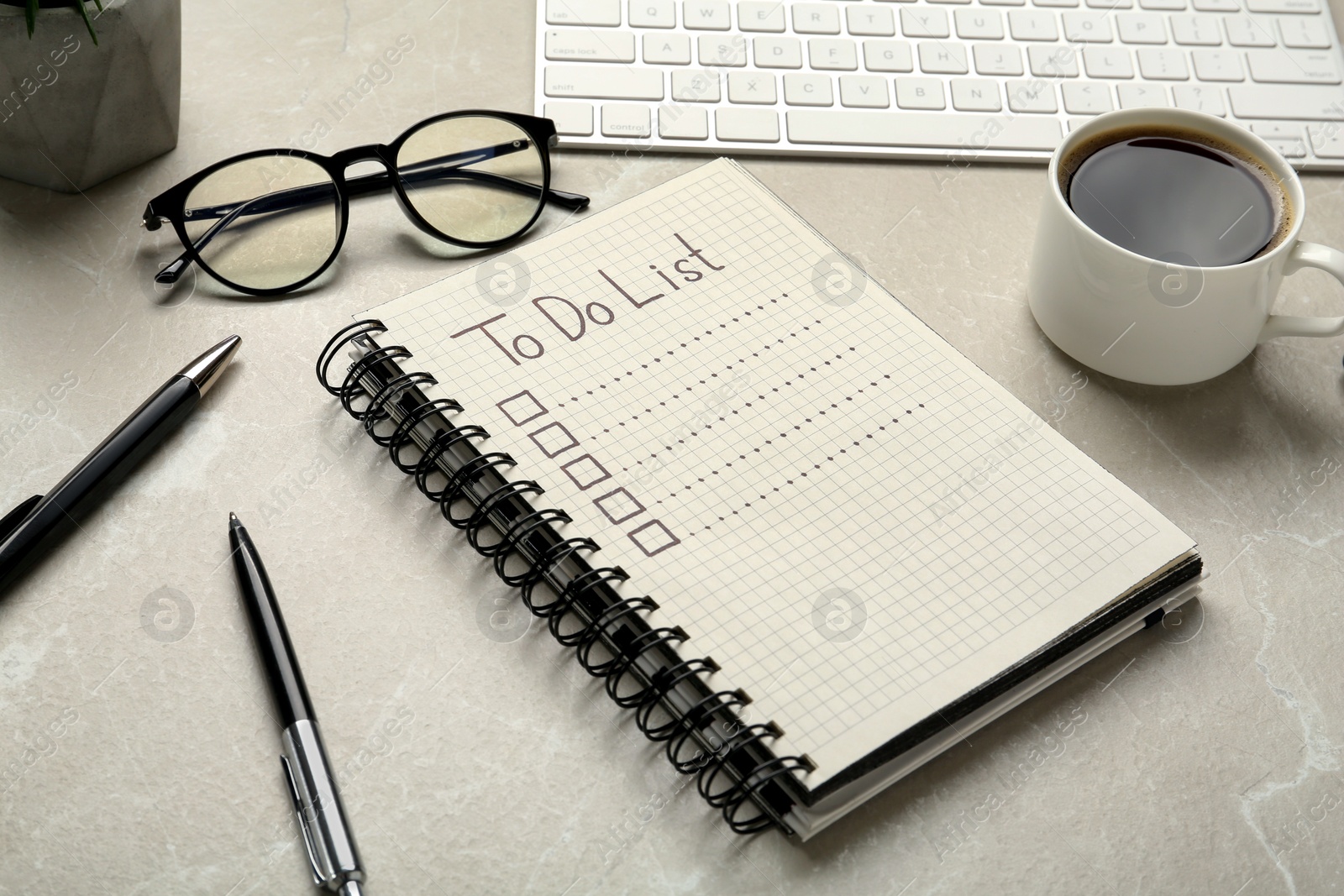 Photo of Notepad with unfilled To Do list, pens, glasses and cup of coffee light on grey marble table