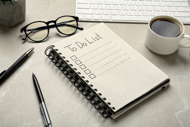 Photo of Notepad with unfilled To Do list, pens, glasses and cup of coffee light on grey marble table
