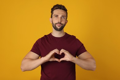 Photo of Man making heart with hands on yellow background
