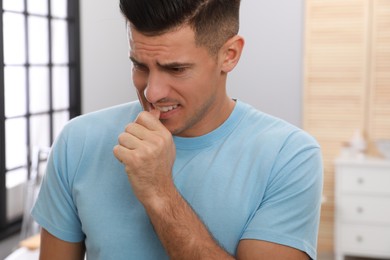 Photo of Man biting his nails indoors. Bad habit