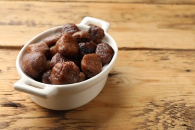 Photo of Roasted edible sweet chestnuts in dish on light wooden table, space for text