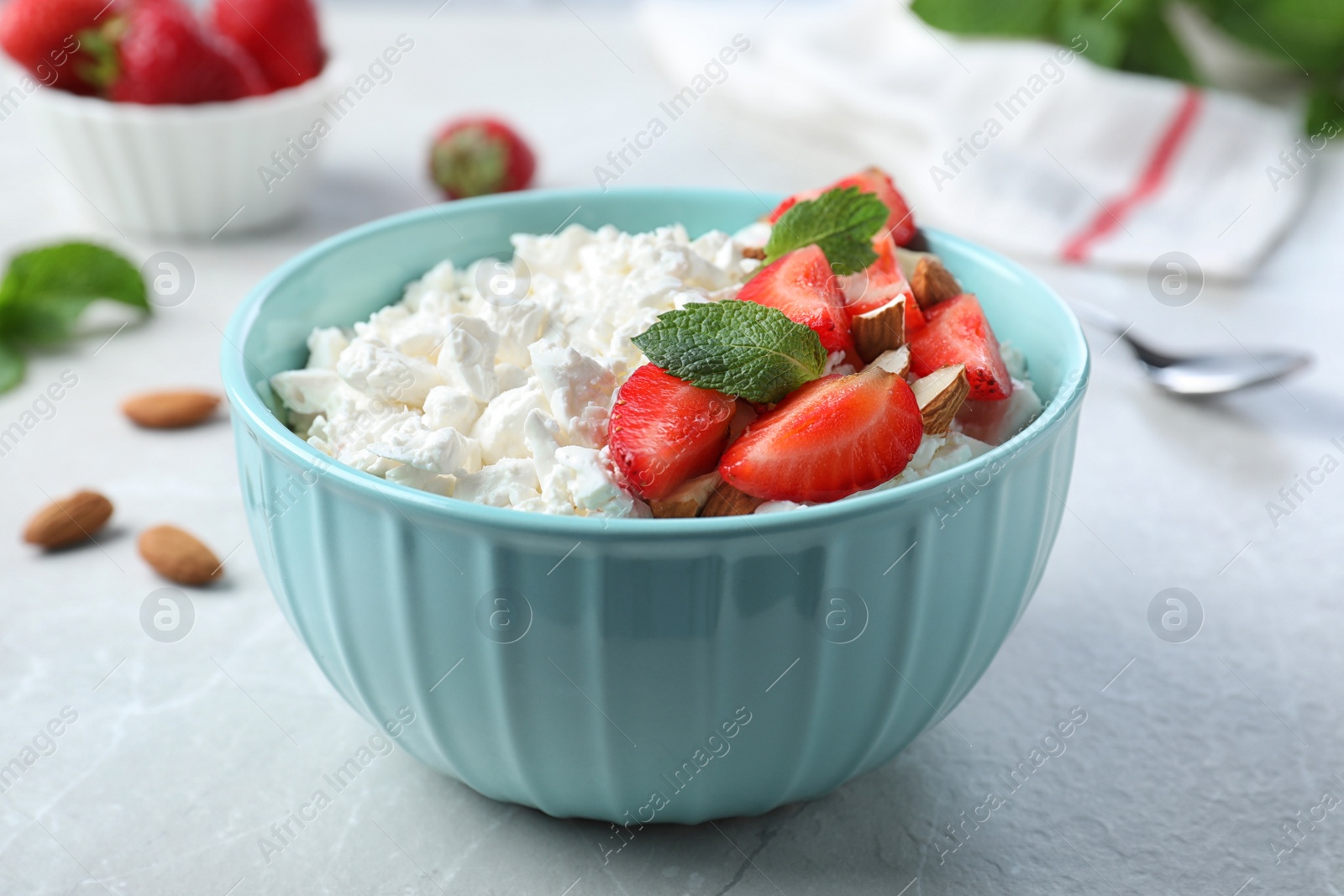 Photo of Fresh cottage cheese with strawberry and almond in bowl on light marble table, closeup