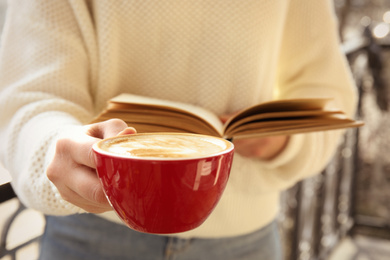 Woman with cup of coffee reading book outdoors, closeup