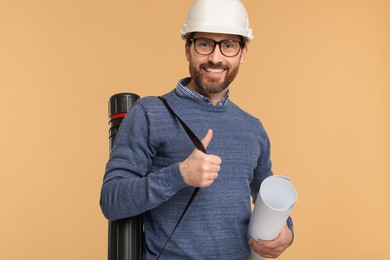 Photo of Architect in hard hat with drawing tube and draft on beige background