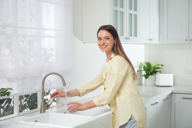 Woman filling glass with water from tap in kitchen
