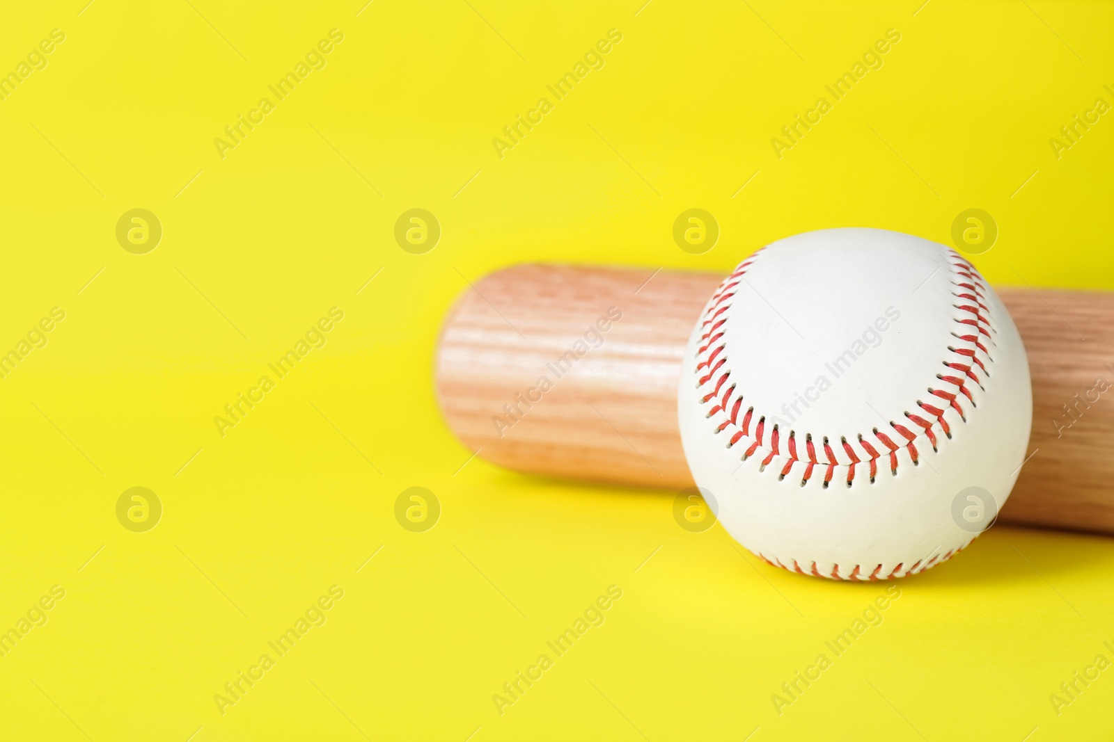 Photo of Wooden baseball bat and ball on yellow background, closeup. Space for text