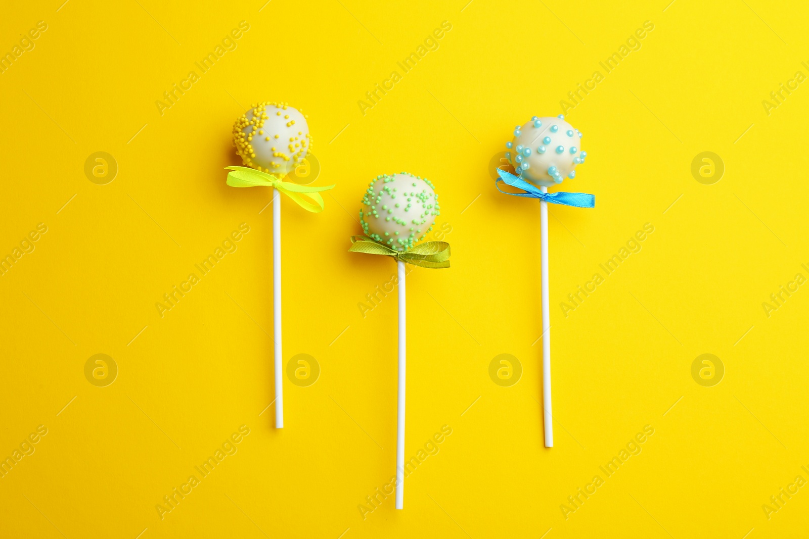 Photo of Different tasty cake pops on yellow background, flat lay