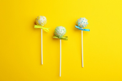 Photo of Different tasty cake pops on yellow background, flat lay