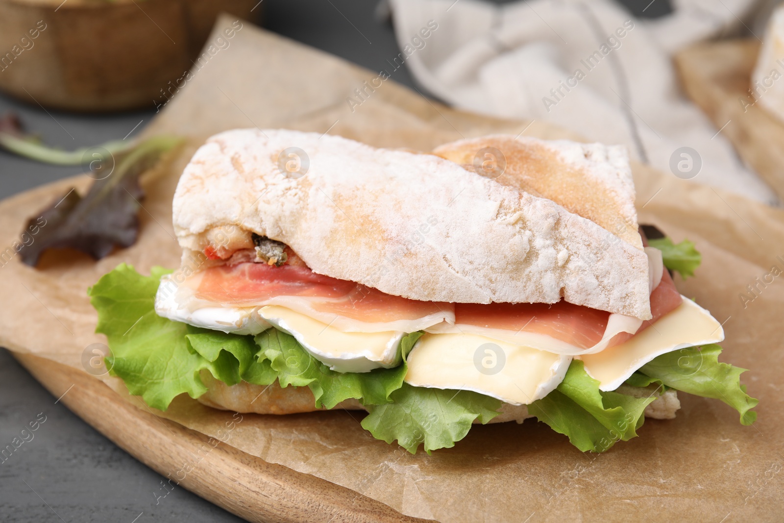 Photo of Tasty sandwich with brie cheese and prosciutto on grey table, closeup