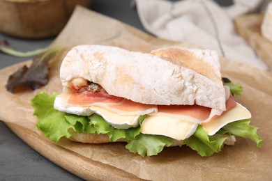 Tasty sandwich with brie cheese and prosciutto on grey table, closeup