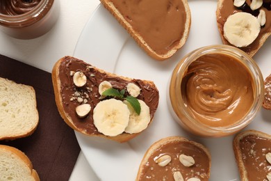 Photo of Toasts with different nut butters, banana slices, blueberries and nuts on white table, flat lay