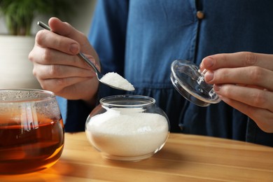 Photo of Woman adding sugar into aromatic tea at wooden table indoors, closeup