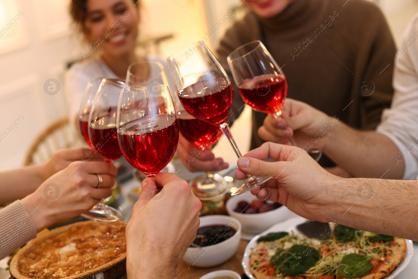 Photo of Group of people clinking glasses with red wine during brunch at table indoors, closeup