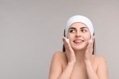 Young woman with headband washing her face on light grey background, space for text